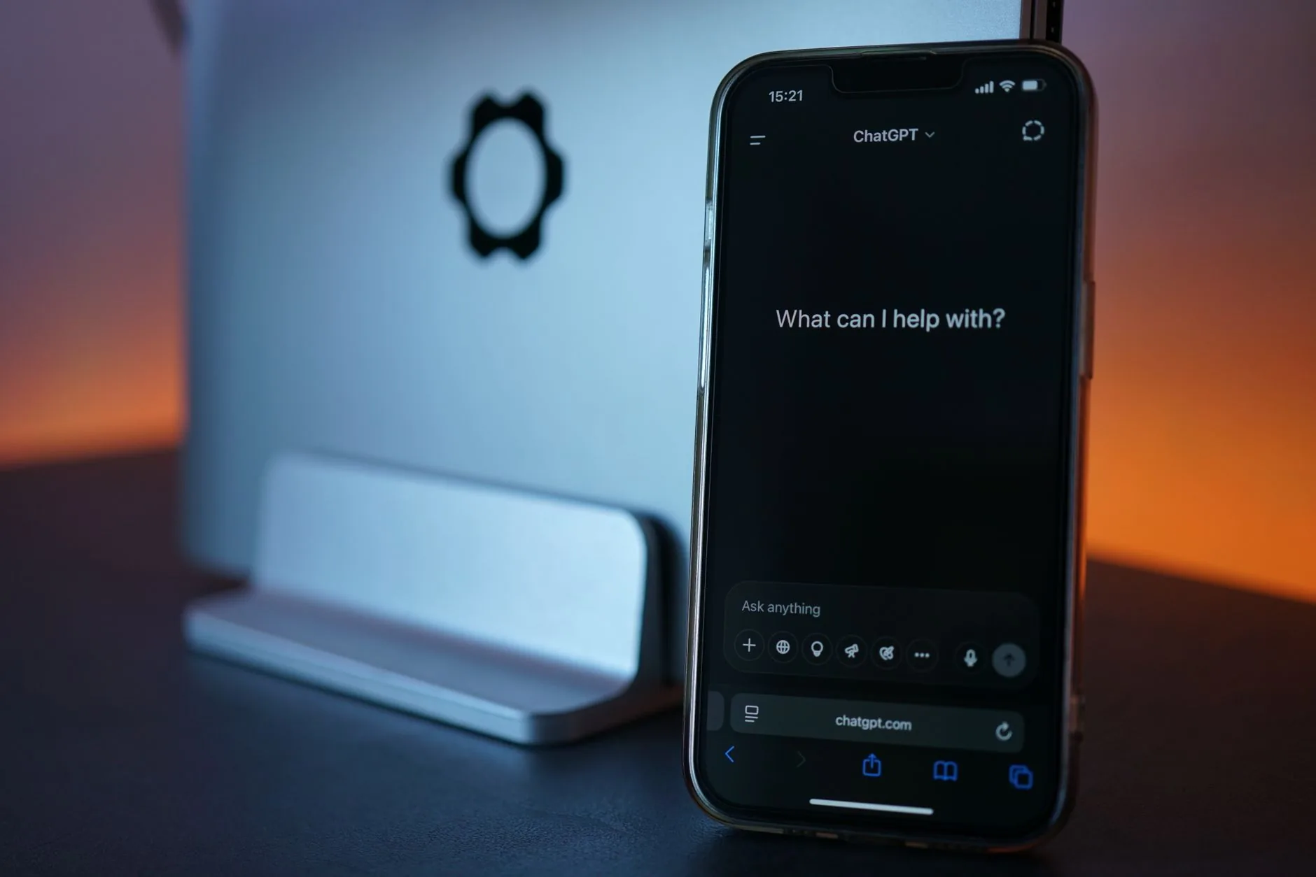 Telemóvel sobre uma secretária a mostrar uma conversa de mensagens, com espaço de trabalho de equipa ao fundo